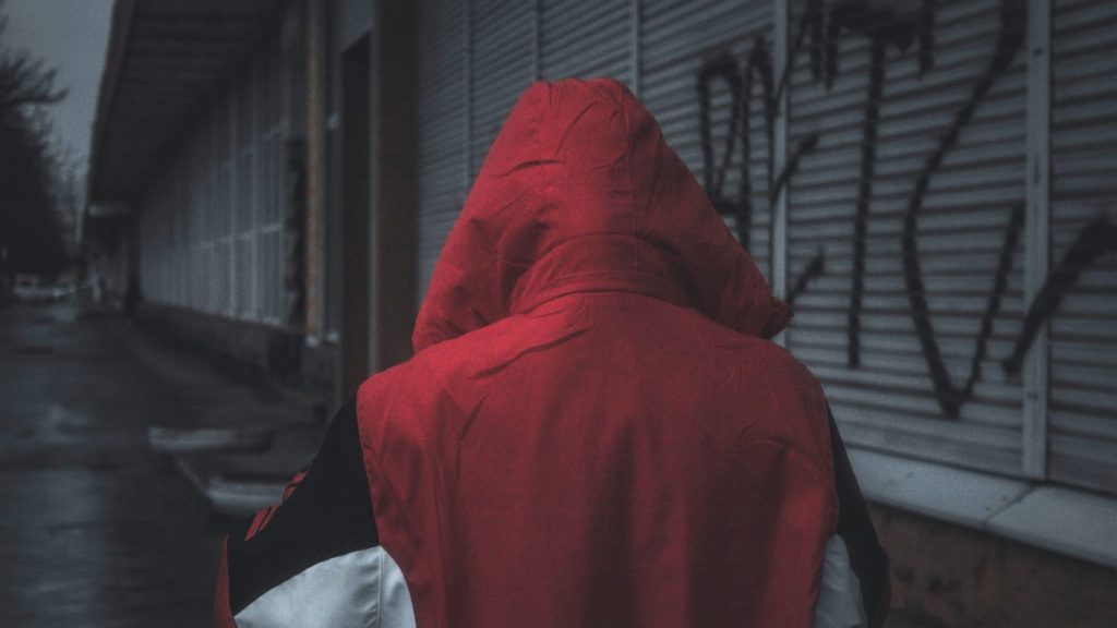 Imagen de una persona encapuchada con un abrigo rojo caminando en un callejón.