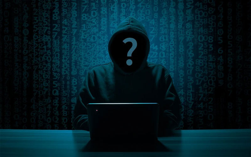 Imagen que muestra una figura desconocida encapuchada (presumiblemente un hacker) sentada frente a una computadora portátil