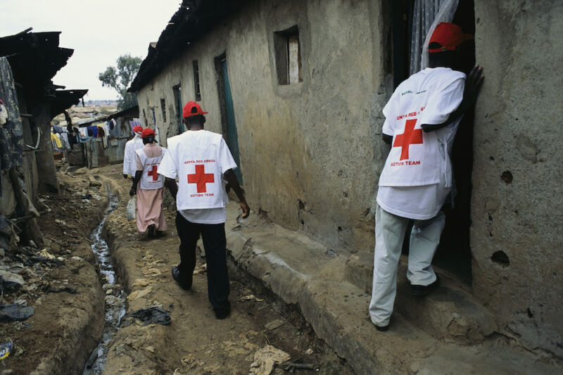 Personas con chalecos de la Cruz Roja caminan por una calle de tierra.