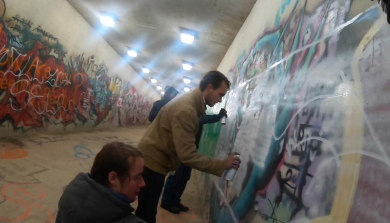 Los hombres usan pintura en aerosol para desfigurar un mural en un túnel público.