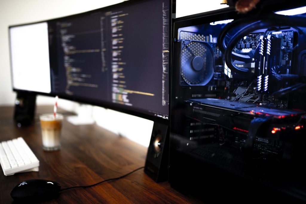 Imagen de un escritorio con dos monitores anchos uno al lado del otro y una torre de PC que está abierta y muestra todos sus componentes.
