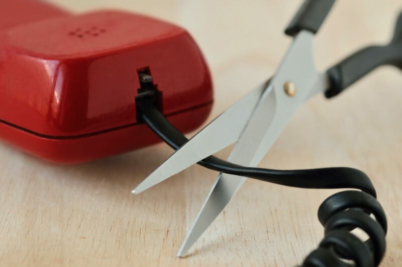 Un par de tijeras que se utilizan para cortar un cable que sale de un teléfono fijo.