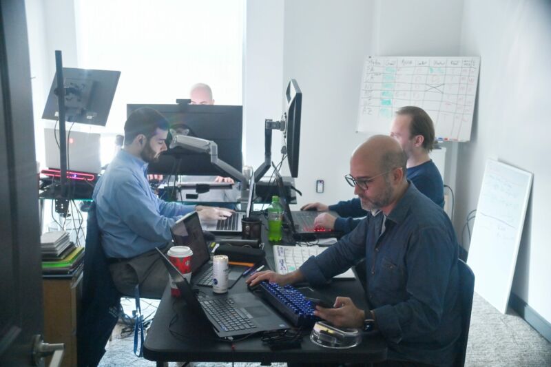 Cuatro hombres sentados frente a computadoras en un lugar de trabajo.