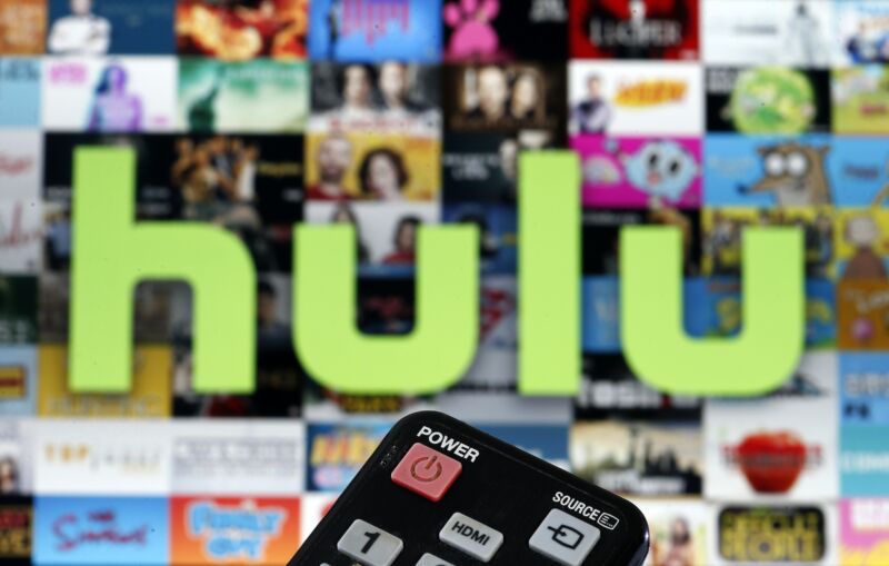 Ilustración fotográfica de un control remoto frente a una pantalla de televisión que muestra contenido de Hulu TV.