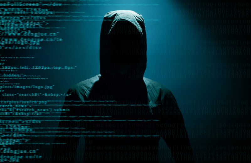 Fotografía de archivo de una figura encapuchada escondida detrás de un código de computadora.