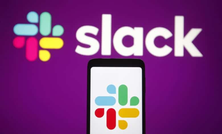 The slack logo on a mobile phone in front of a purple wall with the slack logo on it