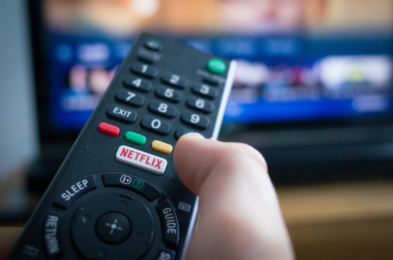 La mano de una persona sosteniendo un control remoto de TV con un botón para Netflix.